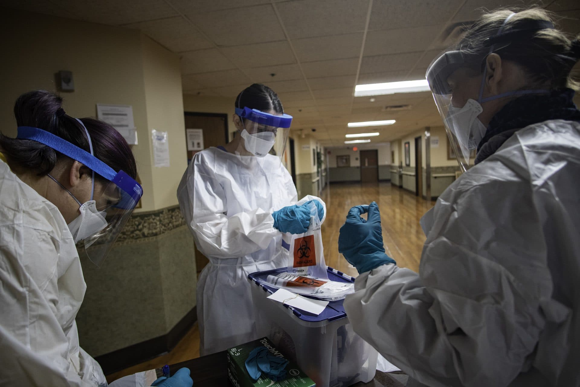 Volunteers in gowns, masks, and gloves prepare COVID-19 test swabs at a table in a skilled nursing facility in Detroit