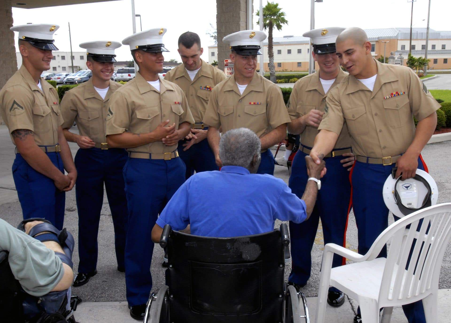 U.S. Marines in dress uniforms speak with an elderly veteran seated in a wheelchair at a Florida state veterans nursing home