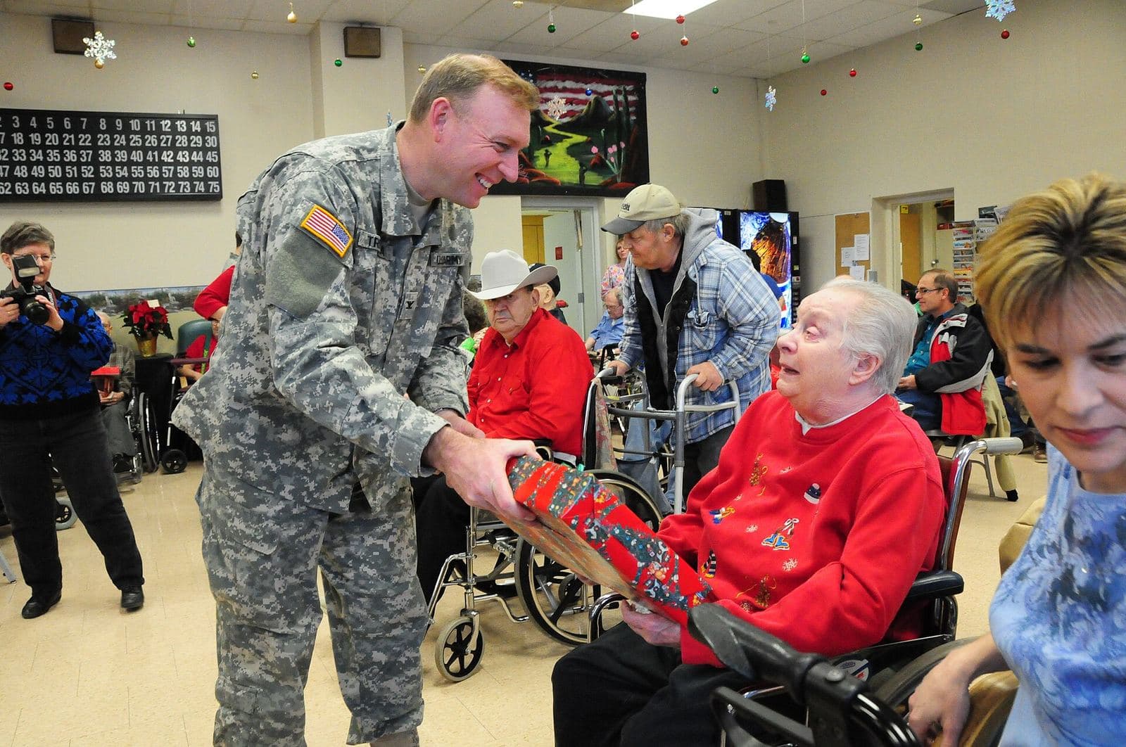 National Guard members in dress uniforms gather with older residents in a veterans nursing home day room